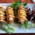 an egg laying on a bed of lettuce divided in 4 packed in ground meat and topped with a savory mustard, called a Scotch Egg.