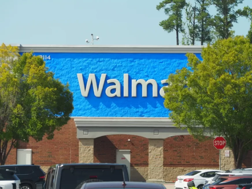 large white letters against a vibrant blue background, the walmart branding on a building, in the foreground are trees and cars, the name is slightly obscured by foliage