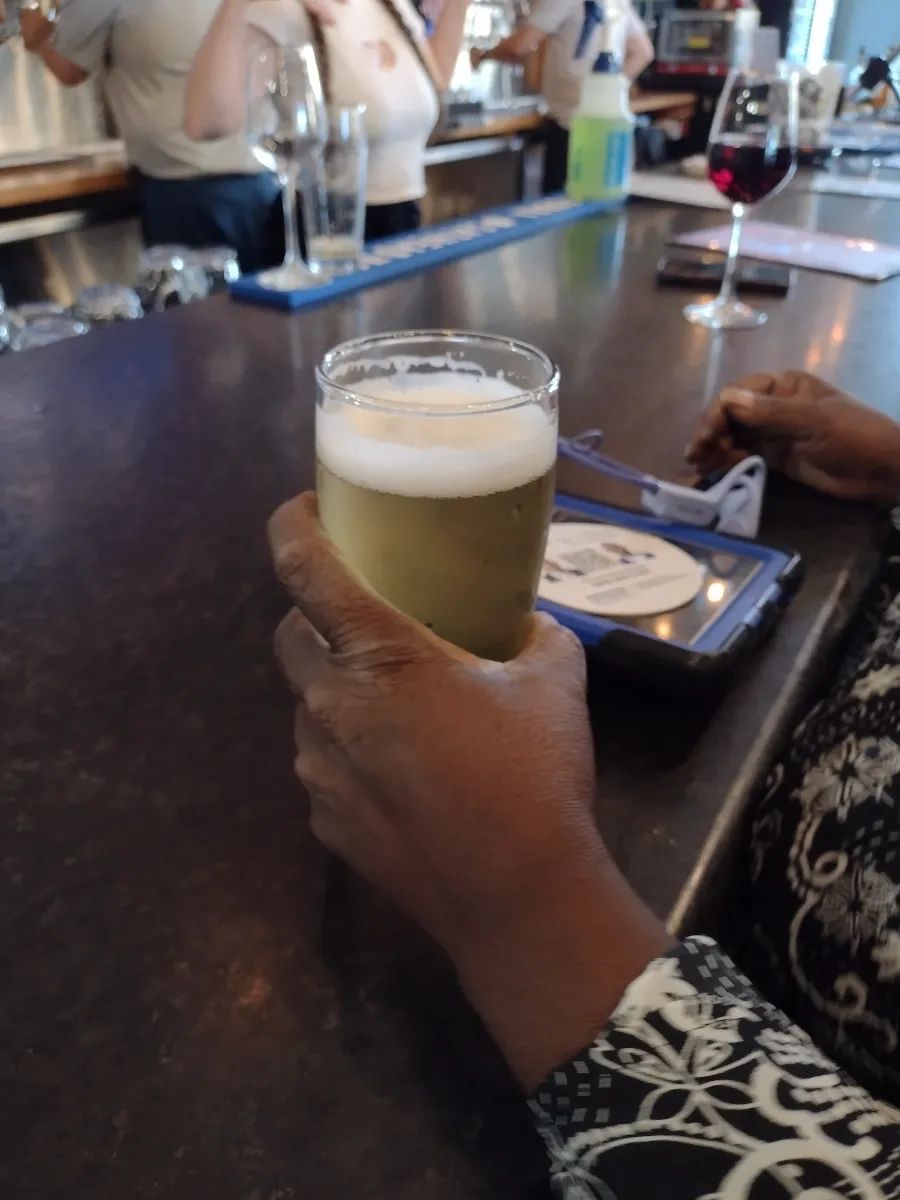 A person holding a glass of light beer at a bar counter