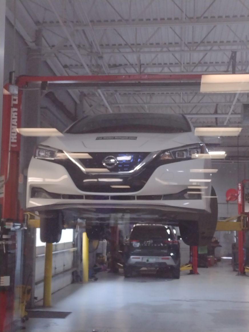 Crossroads Nissan WF – General Inspection White Nissan car raised on a hydraulic lift in an auto repair shop