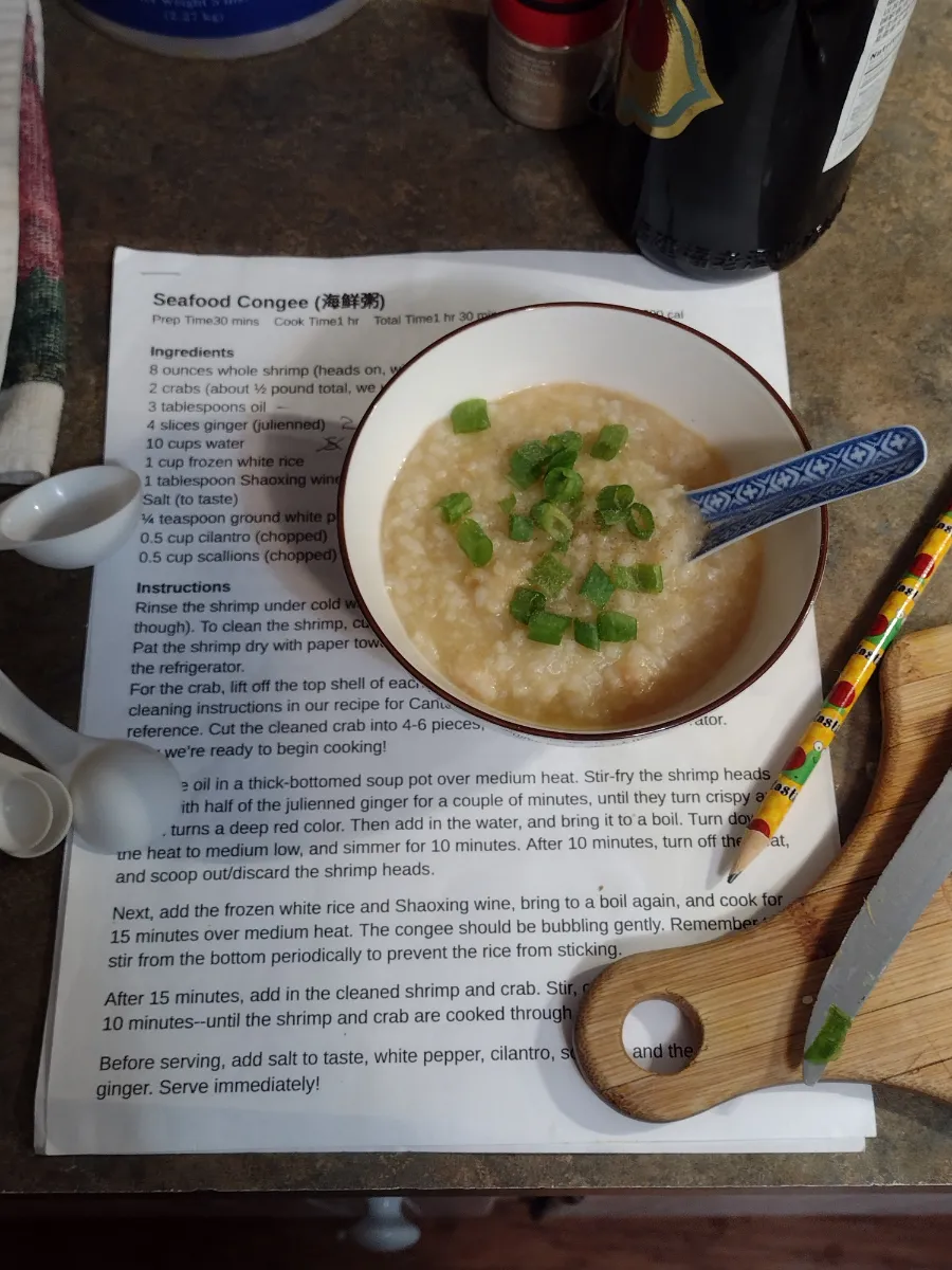 a bowl of seafood congee sprinkled with scallions and seasoned with white pepper