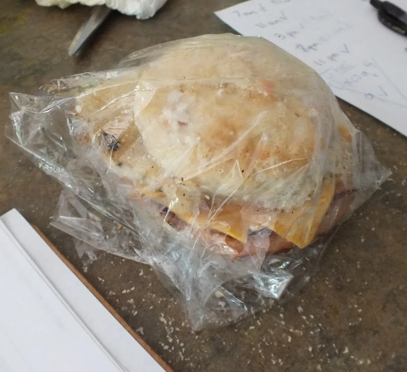 A breakfast sandwich wrapped in clear plastic wrap sitting on a desk