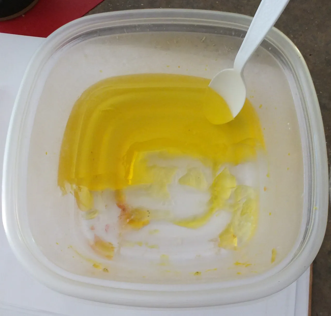 Yellow gelatin in a clear plastic container with a white plastic spoon inside