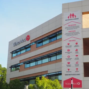 Exterior of a modern WakeMed building with a vertical banner displaying its mission, vision, and goals