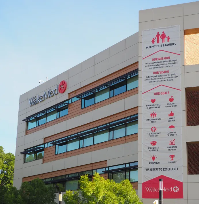 A Successful Operation Exterior of a modern WakeMed building with a vertical banner displaying its mission, vision, and goals