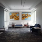 waiting area with several chairs and short tables, a pair of photos hand on the wall depicting the leaves of a Ginko tree, sunlight pours in from windows on either side of the hall.