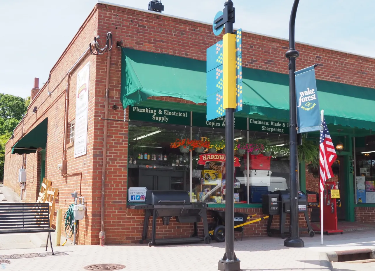 Brick hardware store with green awnings, barbecue grills, and a Wake Forest Downtown banner outside