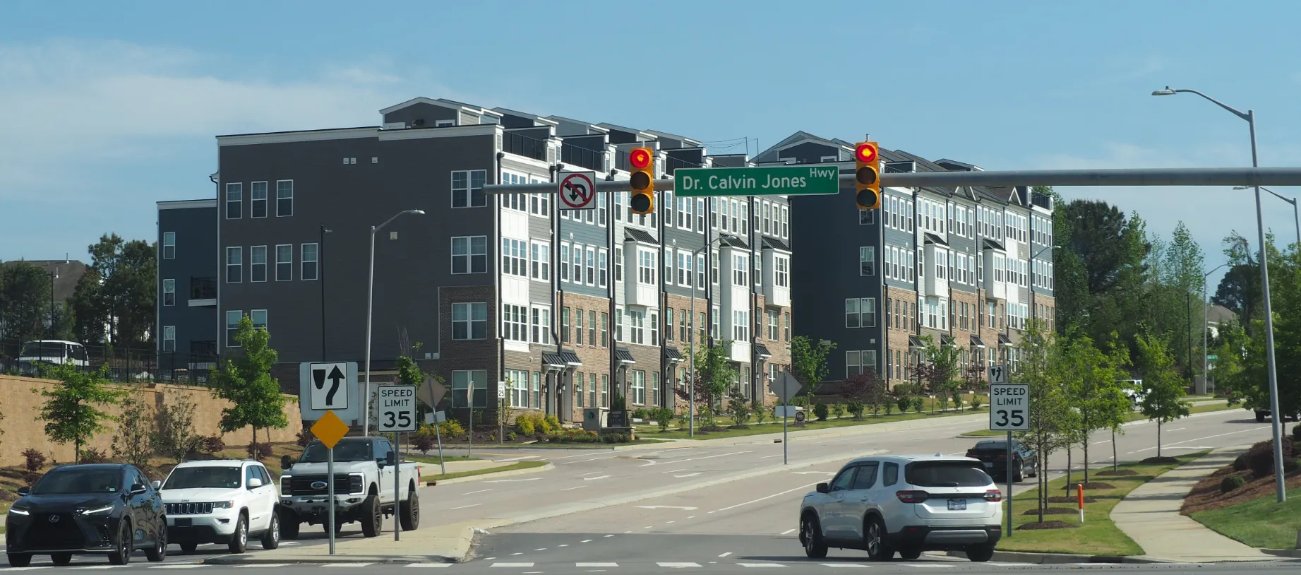 Cars stopped at a red light on Dr. Calvin Jones Highway with modern multi-story apartment buildings in the background