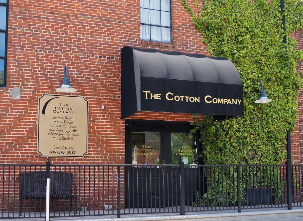 Red brick storefront of The Cotton Company featuring a black awning, ivy-covered wall, and directory sign
